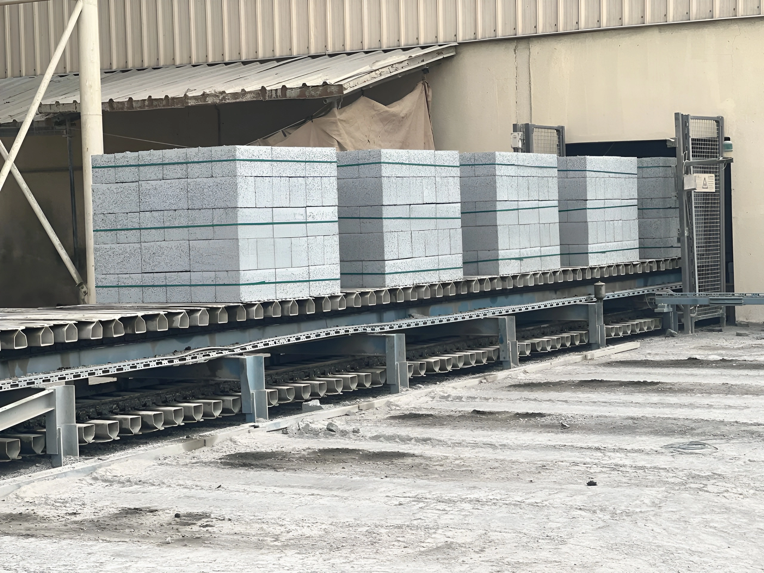 Stacked concrete block pallets on production conveyor inside factory